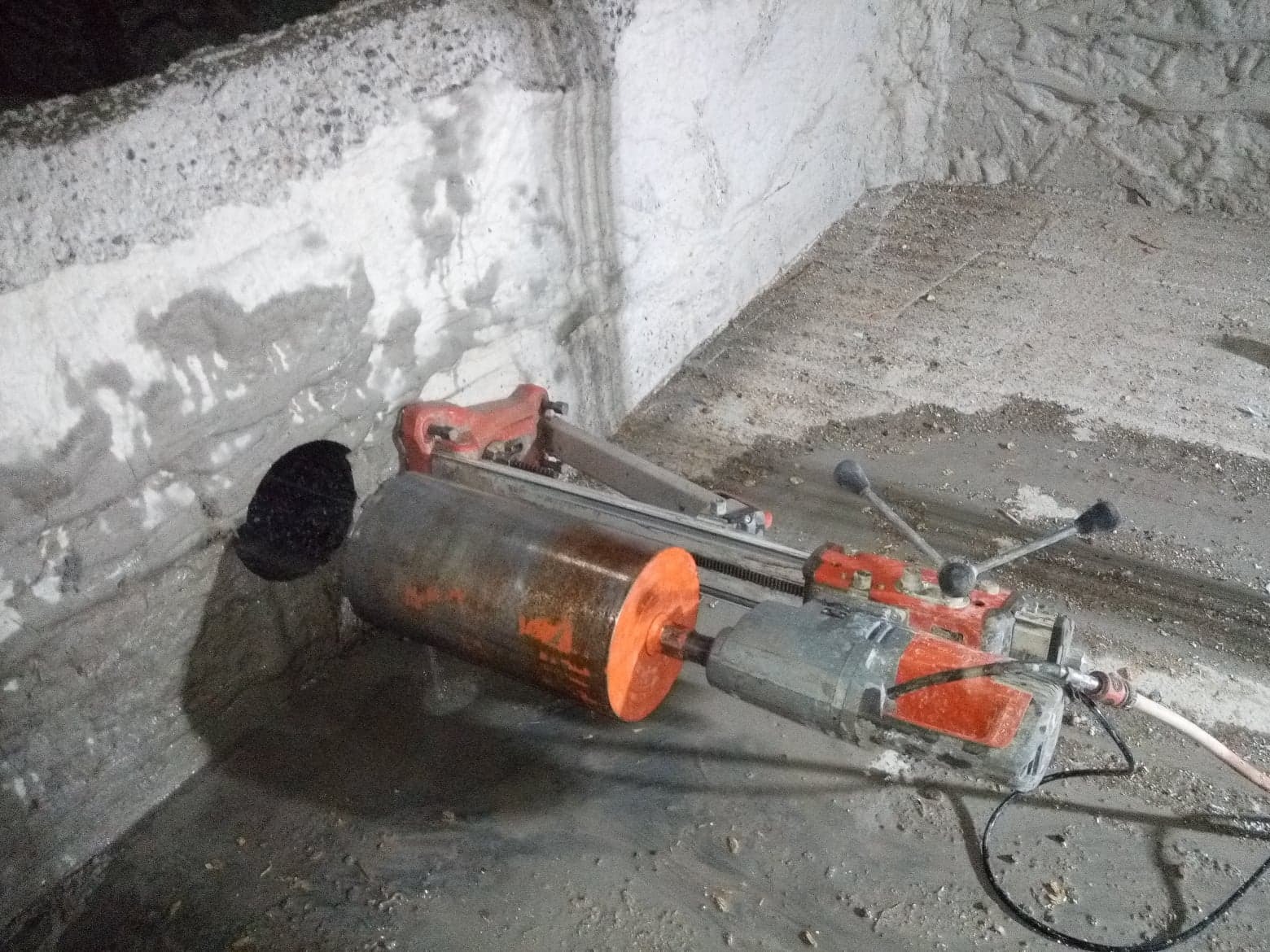 Wiertnica diamentowa wykonuje otwór w betonowej ścianie, widoczne ślady wody po wierceniu.