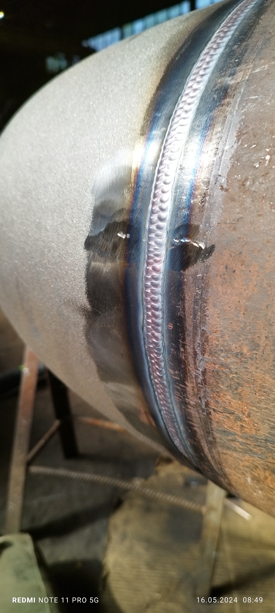 Spoina na metalowej rurze, widoczne tęczowe przebarwienia po procesie łączenia, zarysowania na powierzchni rury.