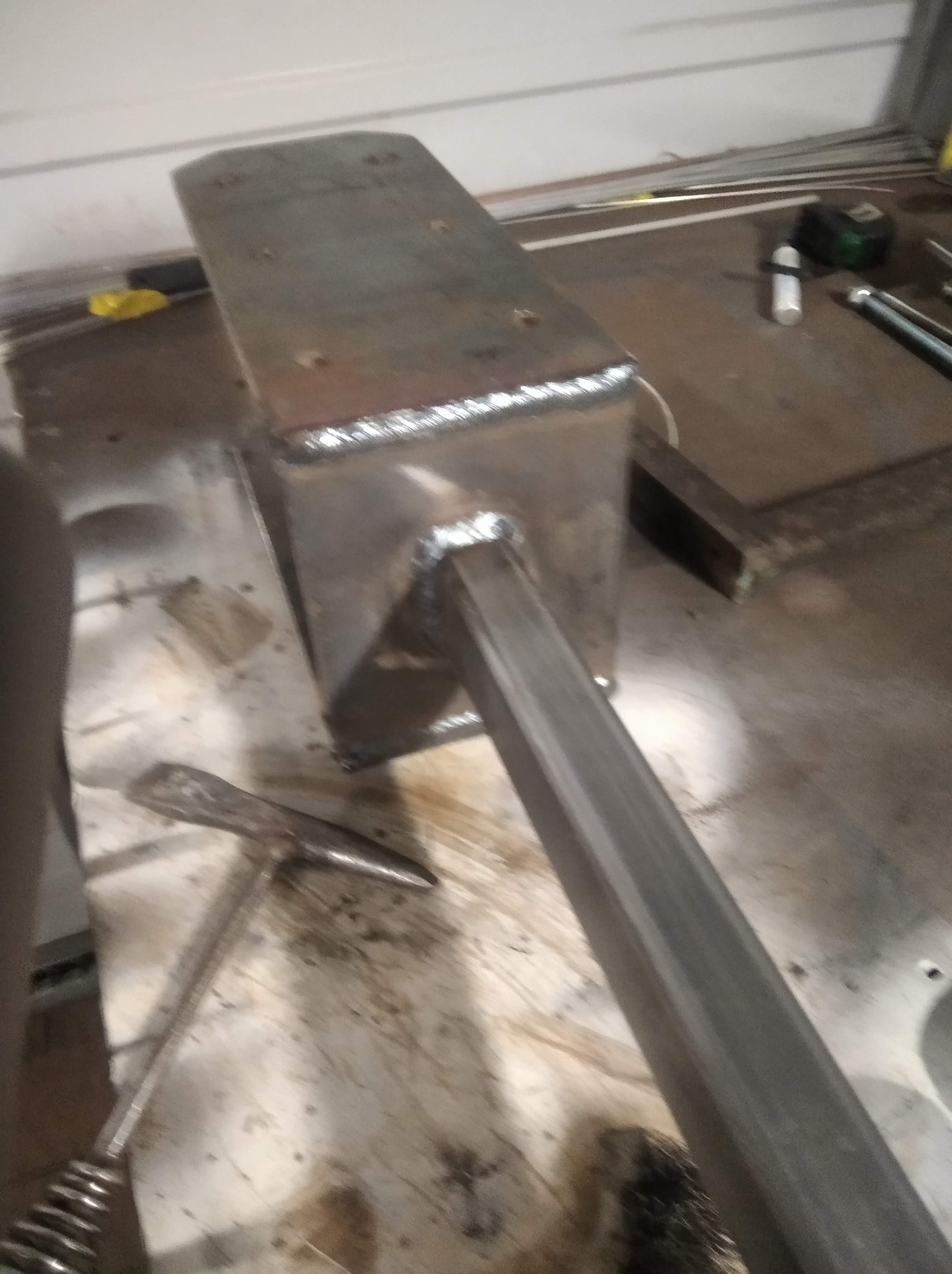 Metalowa konstrukcja spawana z profili zamkniętych, widoczne spoiny, młotek ślusarski i inne narzędzia na stole warsztatowym.