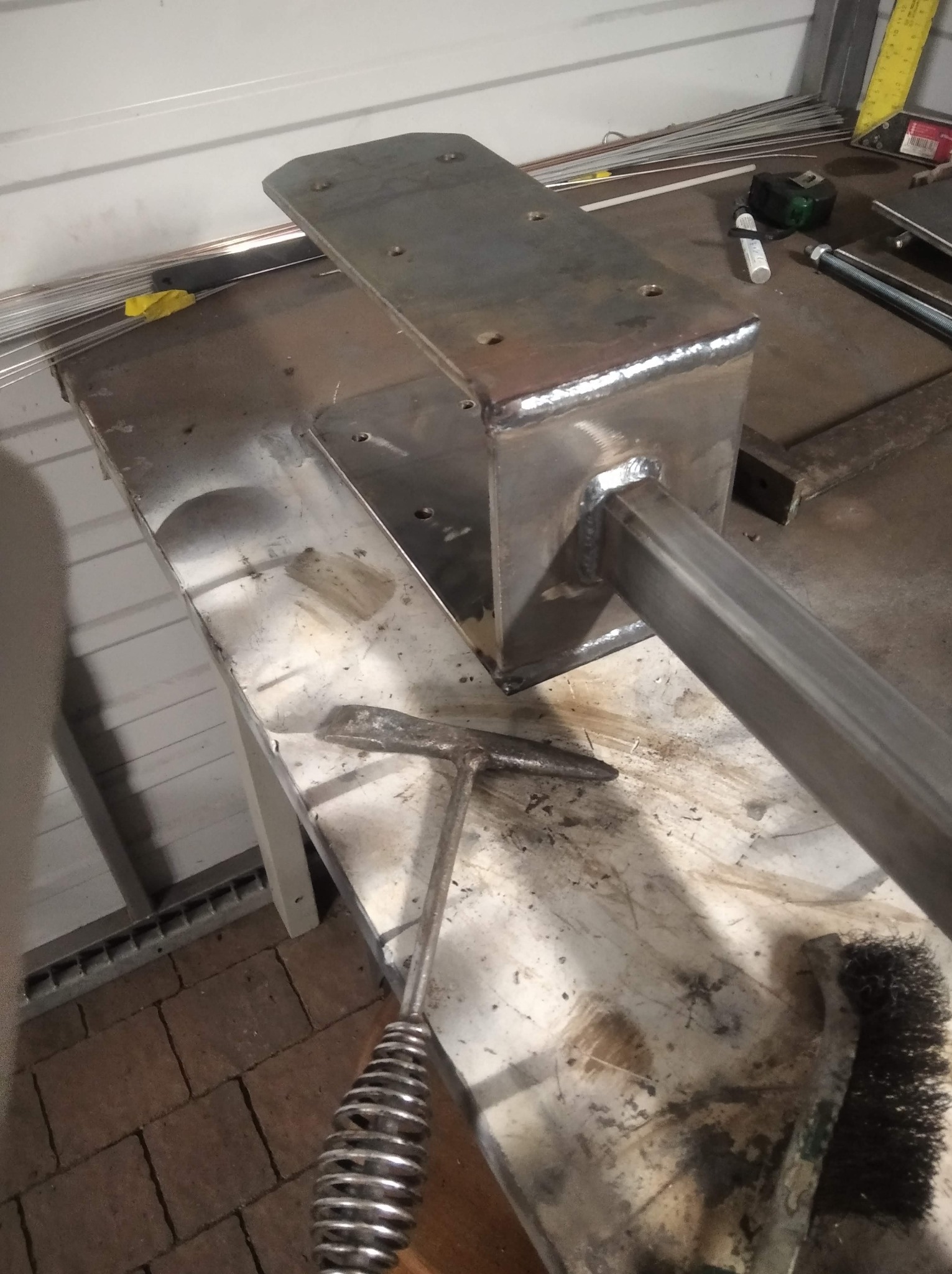 Metalowa konstrukcja spawana z profili, widoczne spoiny, na stole roboczym leży młotek spawalniczy i szczotka druciana.