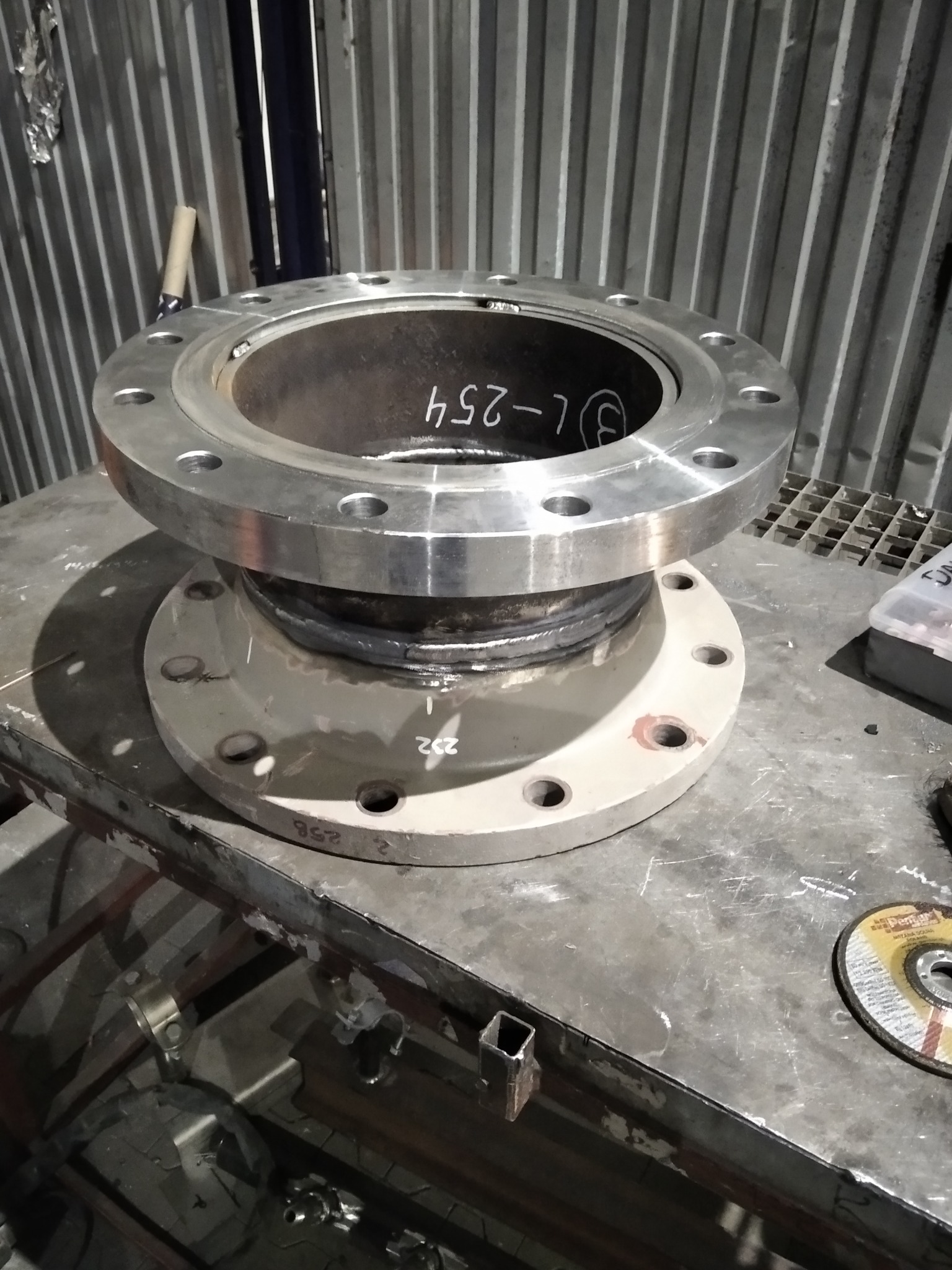 Zespawane, metalowe kołnierze na stole warsztatowym z widocznymi śladami po spawaniu i oznaczeniami na wewnętrznej stronie rury.