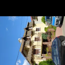 Żółty dom z odsłoniętą konstrukcją dachu podczas prac, widoczny samochód osobowy i dostawczy na ulicy.