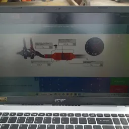 Diagnostyka DPF na laptopie Acer, widoczne parametry regeneracji filtra cząstek stałych, w tle maszyny budowlane.