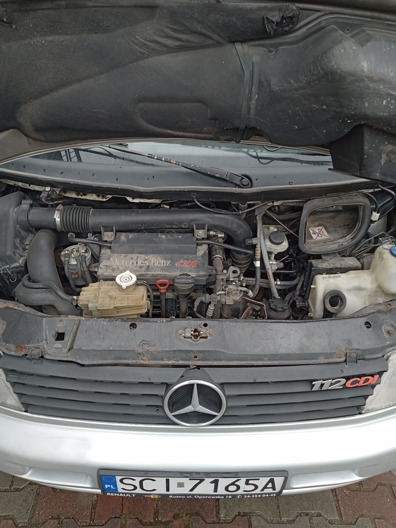 Otwarta maska samochodu Mercedes Benz 112 CDI, widoczny silnik, elementy instalacji elektrycznej i płynów eksploatacyjnych, tablica rejestracyjna z przodu pojazdu.