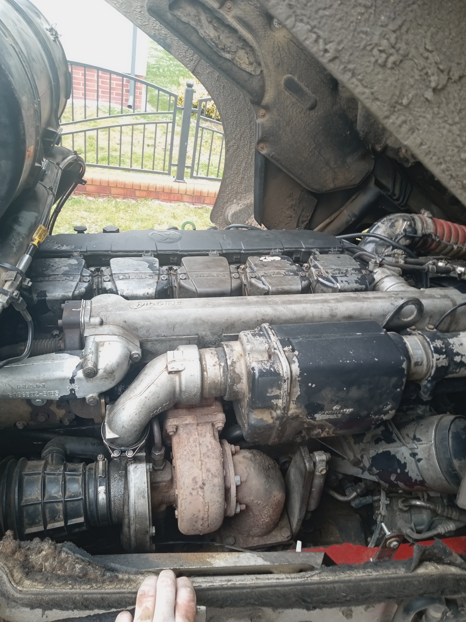 Otwarty silnik MAN w samochodzie ciężarowym, widoczne turbosprężarka i przewody, zabrudzenia eksploatacyjne.