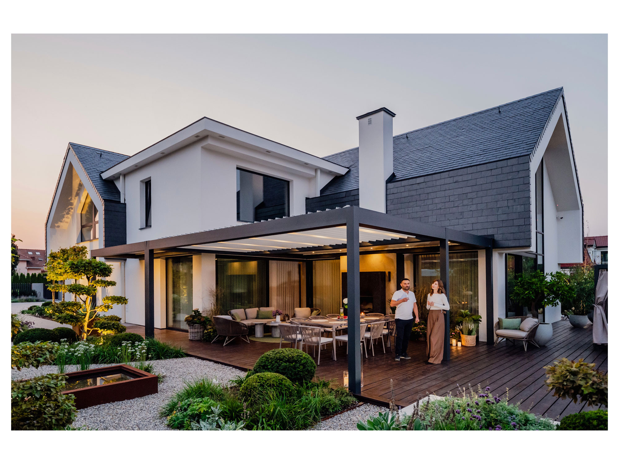 Nowoczesny ogród z drewnianym tarasem, pergolą i oświetleniem, idealny do relaksu. Para z kieliszkami wina dodaje scenie życia i elegancji. Kameralna atmosfera.