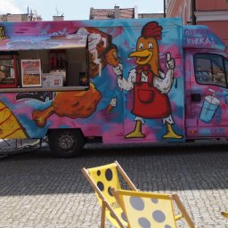 Gastro Faza Sp.zoo - Kolorowy food truck z rysunkiem kurczaka i napisem 'Chrupiąca Kurka' na tle miejskiego placu z żółtymi leżakami.