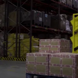 Magazyn z pracownikami transportującymi zapakowane kartony z odzieżą na paletach i w żółtych kontenerach.