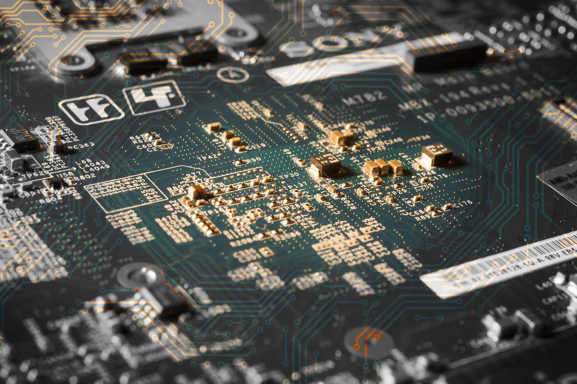 Zbliżenie na płytę główną z widocznymi elementami elektronicznymi, ścieżkami i oznaczeniami, oświetlona w sposób podkreślający szczegóły, ukazująca skomplikowaną strukturę obwodu drukowanego.