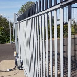 A.R KUDZIA,Schilderbedrijf - Automatyczna brama przesuwna z szarymi pionowymi prętami i czarnymi, ukośnie ściętymi elementami na górze, widoczny mechanizm napędowy i betonowa podstawa.