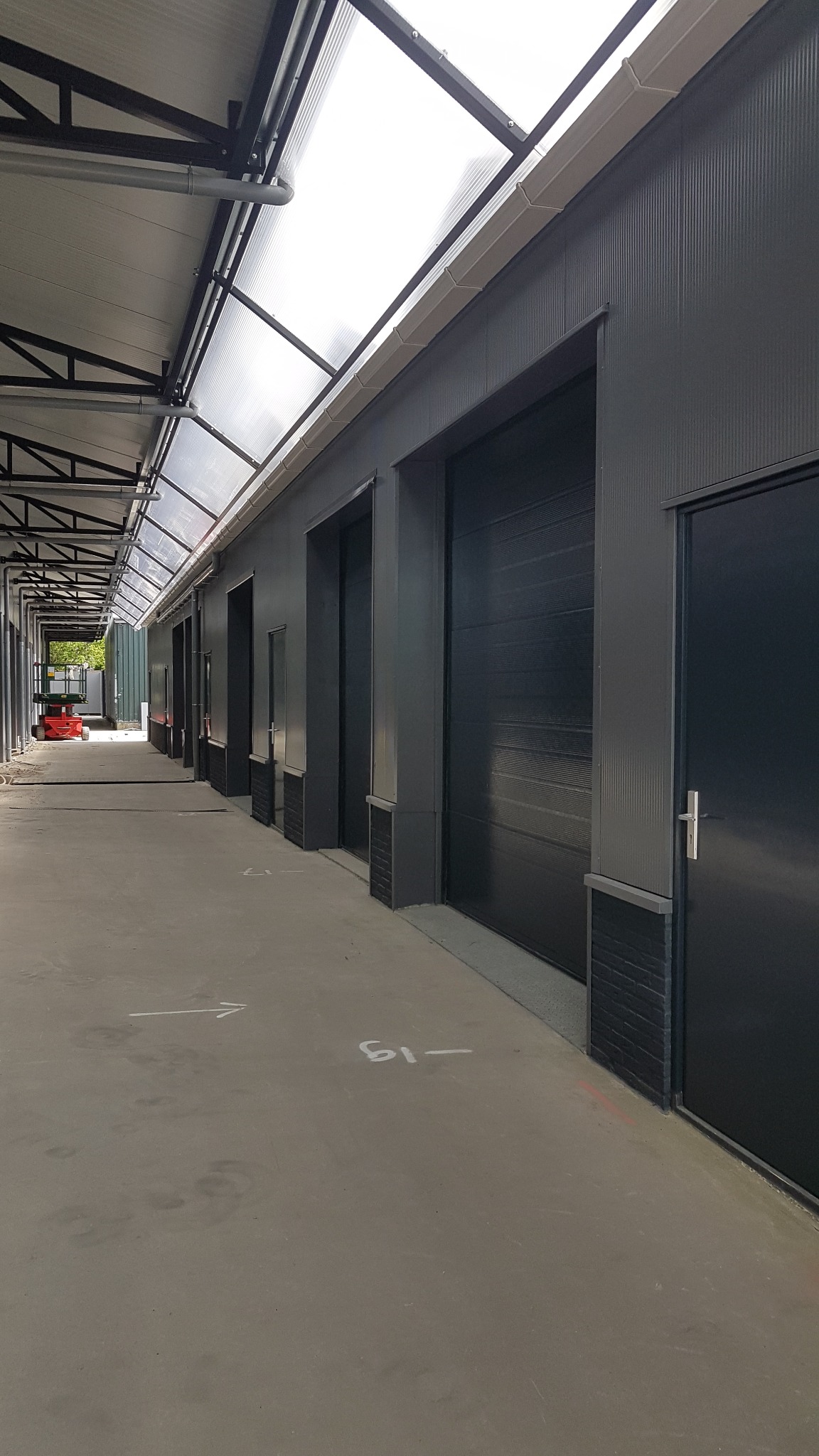 Szary budynek magazynowy z bramami segmentowymi w Głubczycach, widoczne strzałki i numeracja na posadzce, oświetlenie górne.