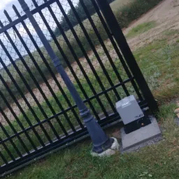 Czarna brama z automatyką FAAC 740 na betonowym fundamencie, widok z bliska na mechanizm i słup, trawa w tle.