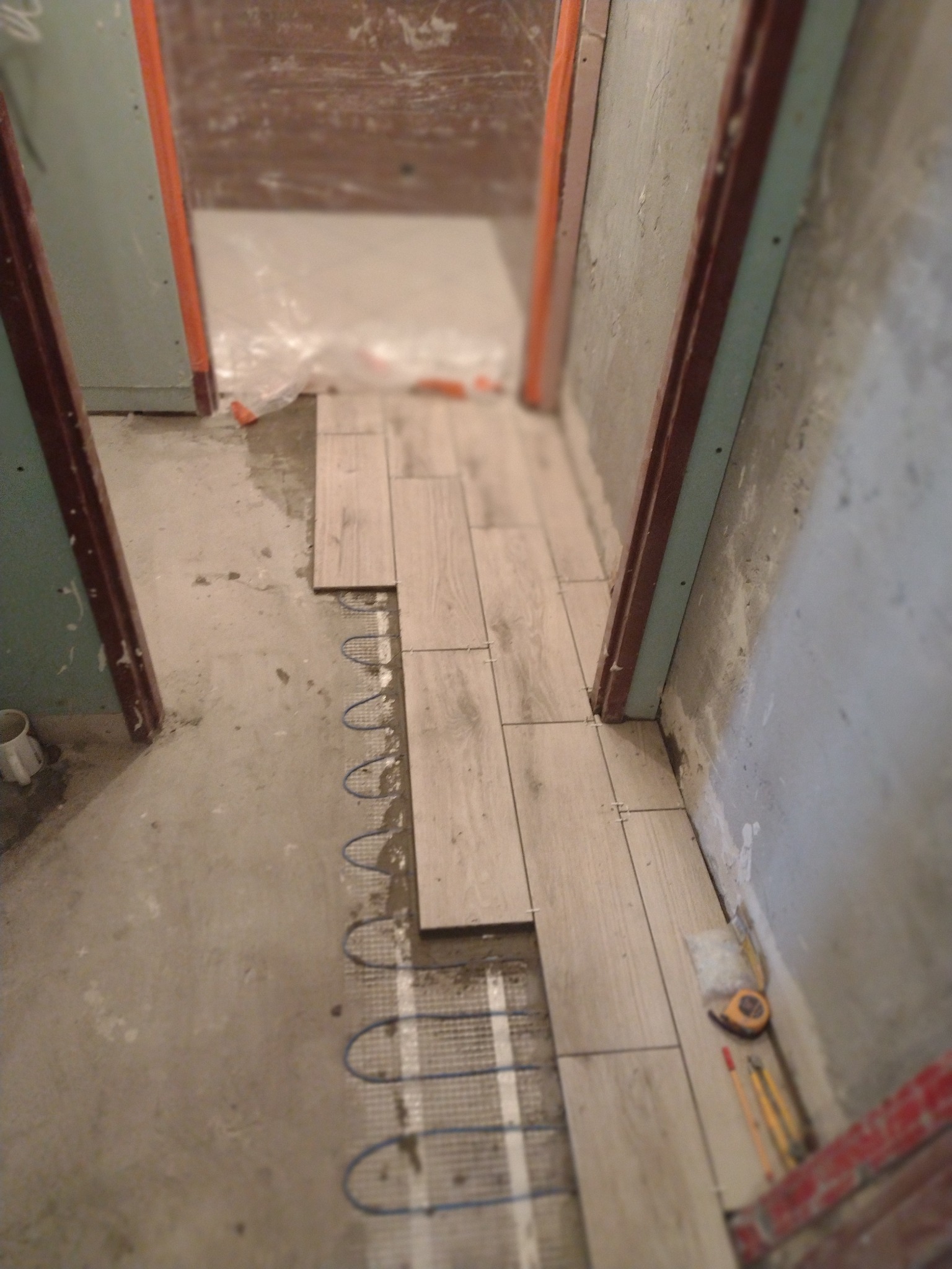 Układanie jasnych płytek podłogowych na ogrzewaniu podłogowym w trakcie remontu, widoczne narzędzia i krzyżyki dystansowe.