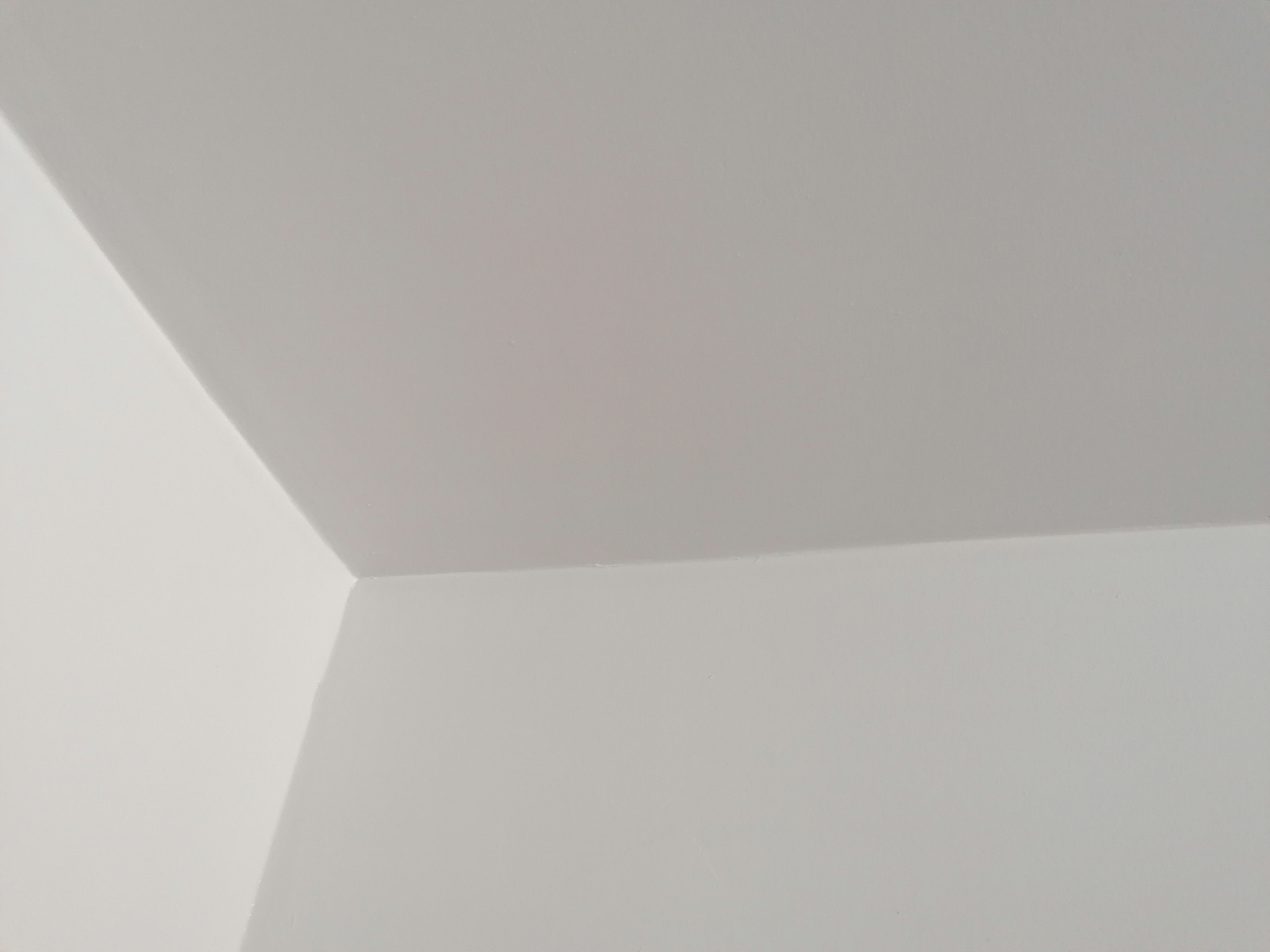 Gładka, świeżo pomalowana na biało ściana i sufit w rogu pomieszczenia, widoczne delikatne cienie.