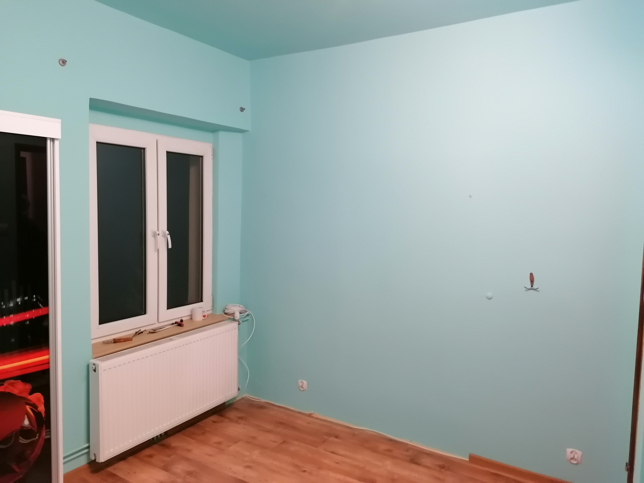 Pokój po odświeżeniu ścian na kolor miętowy, widoczny biały grzejnik pod oknem i drewniana podłoga.