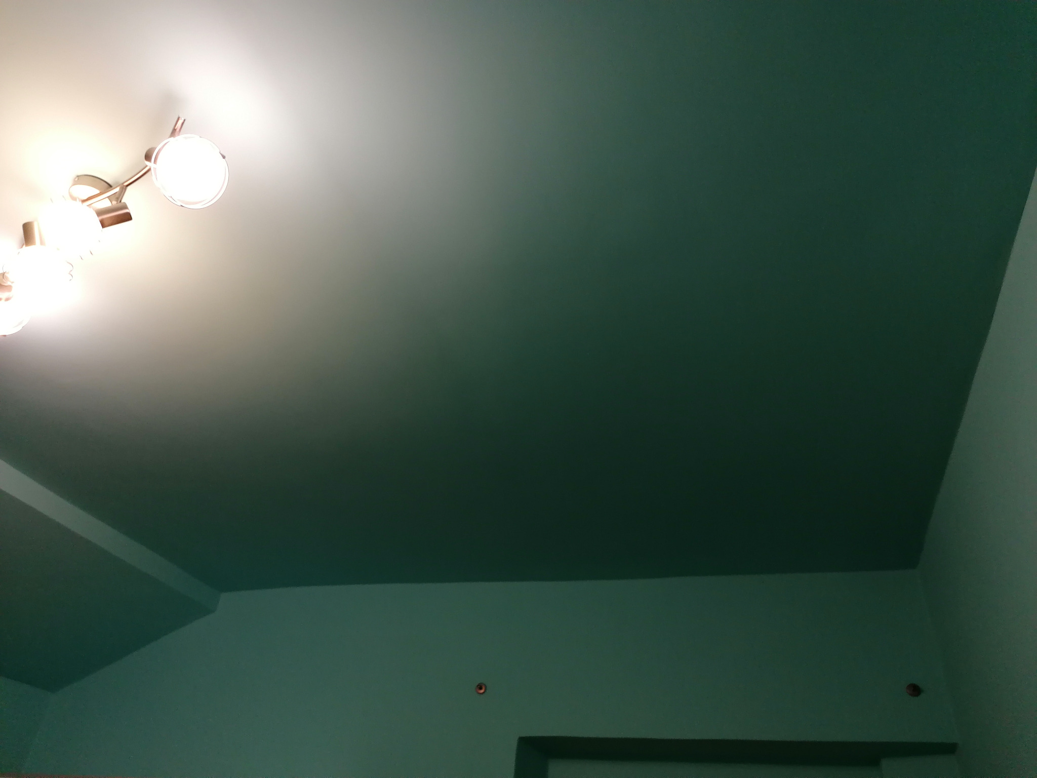 Pomieszczenie z pomalowanym na zielono sufitem i ścianami, oświetlone lampą sufitową z kilkoma reflektorami.