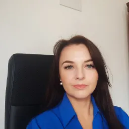 Portret kobiety w niebieskiej koszuli siedzącej na czarnym krześle biurowym w Tarnowie, z certyfikatem widocznym na ścianie w tle.