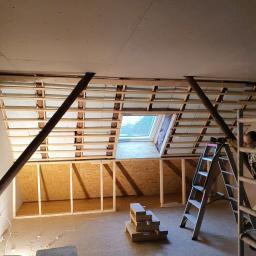 Michael - Poddasze w trakcie adaptacji: widoczne krokwie, izolacja, płyty kartonowo-gipsowe na suficie, okno dachowe, fragment ściany z płyt OSB, drabina i narzędzia pracy.