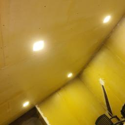 Michael - Wnętrze w trakcie prac wykończeniowych; ściany i sufit pokryte gładzią szpachlową, widoczne otwory pod oświetlenie punktowe w suficie, krzesło w rogu pomieszczenia.