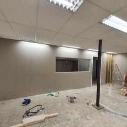 Michael - Wnętrze biura w trakcie remontu: sufit podwieszany kasetonowy, ściany z płyt gipsowo-kartonowych z oknem, widoczne narzędzia i materiały budowlane, podłoga częściowo zabezpieczona.