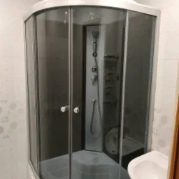 Narożna kabina prysznicowa z hydromasażem i ciemnymi szybami w jasnej łazience z wzorzystymi płytkami.