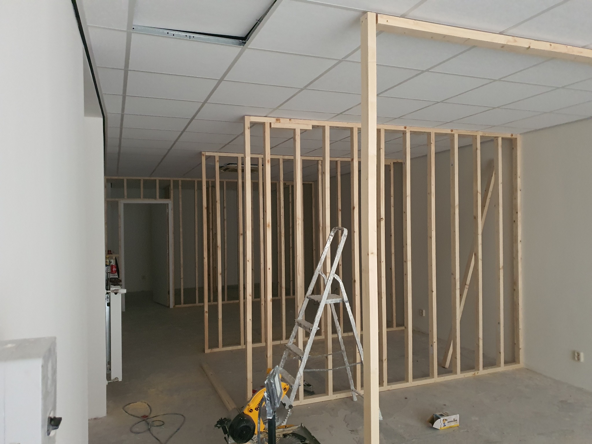 Wnętrze biura w trakcie remontu, widoczne drewniane stelaże ścian działowych, drabina i piła ukośnica.