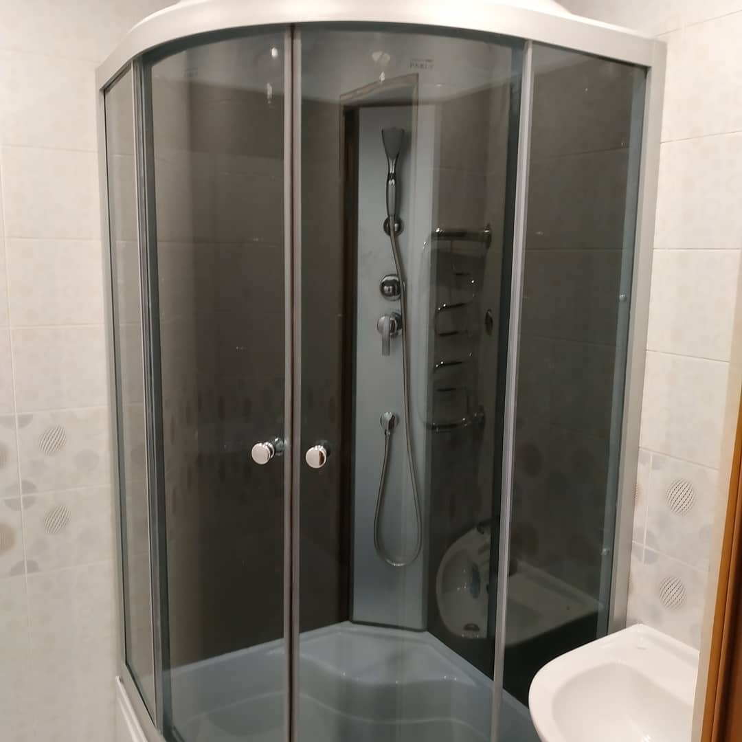 Narożna kabina prysznicowa z hydromasażem i ciemnymi szybami w jasnej łazience z wzorzystymi płytkami.