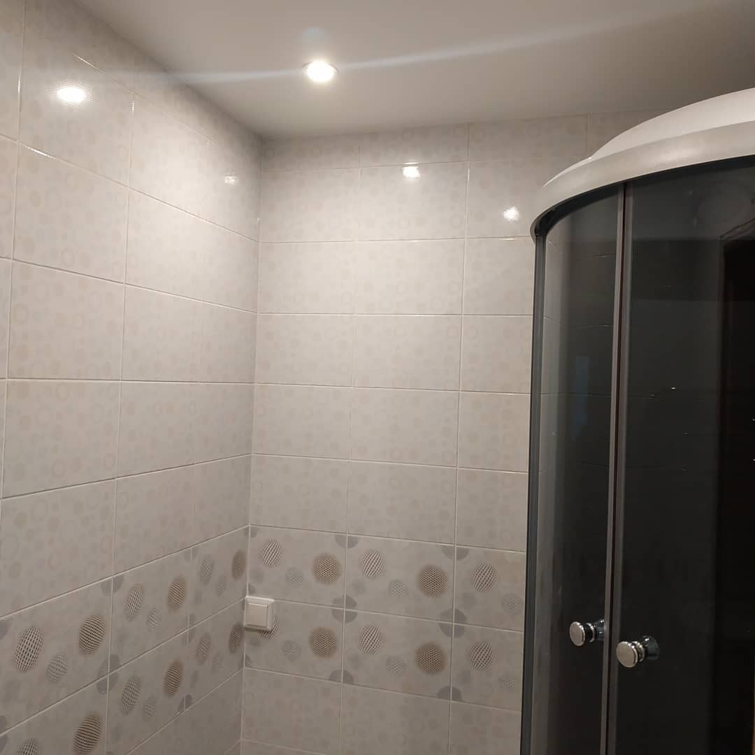 Wykończona łazienka z kabiną prysznicową narożną i jasnymi płytkami ceramicznymi z wzorem w dolnej części ściany.