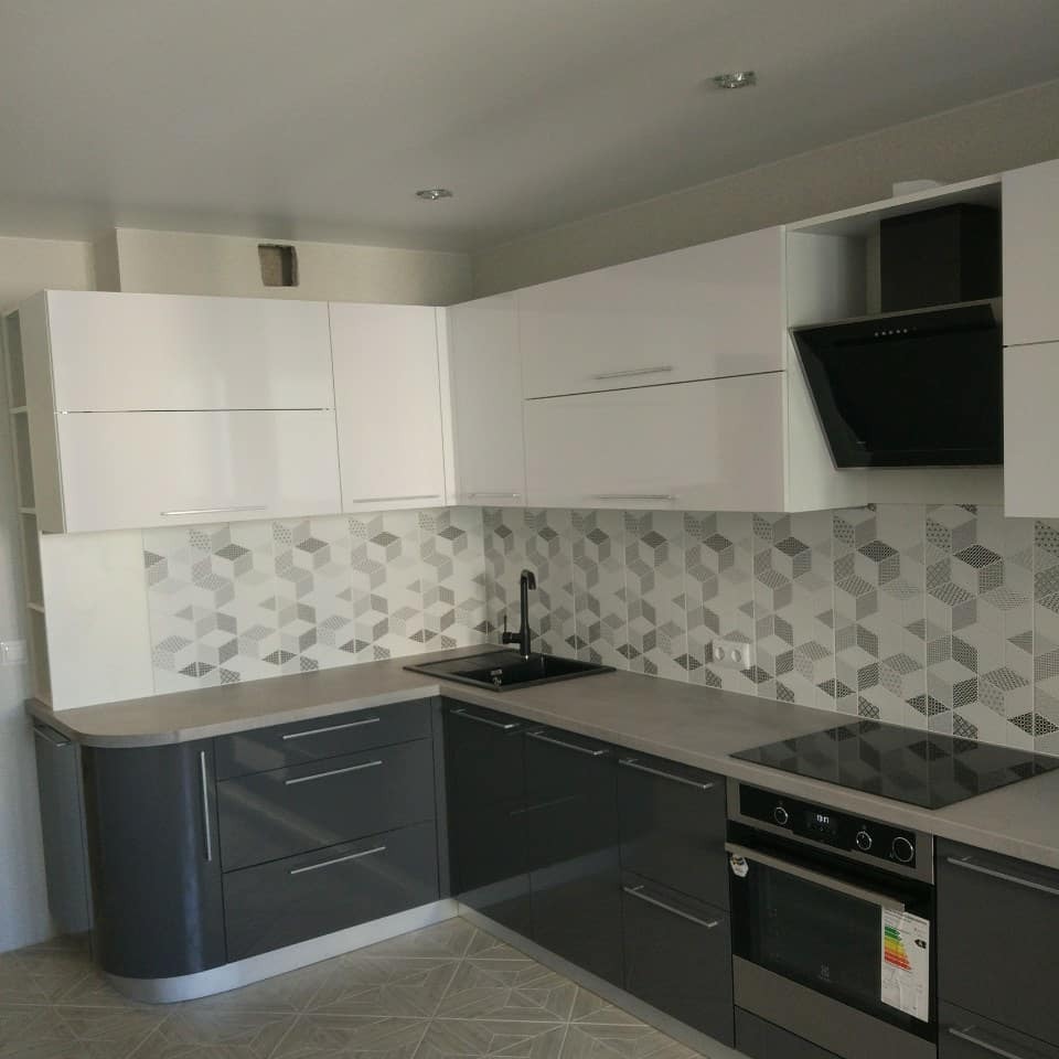 Nowoczesna kuchnia z białymi szafkami górnymi i grafitowymi dolnymi, szary blat, geometryczne płytki nad blatem, czarny zlew i bateria, płyta indukcyjna i piekarnik.