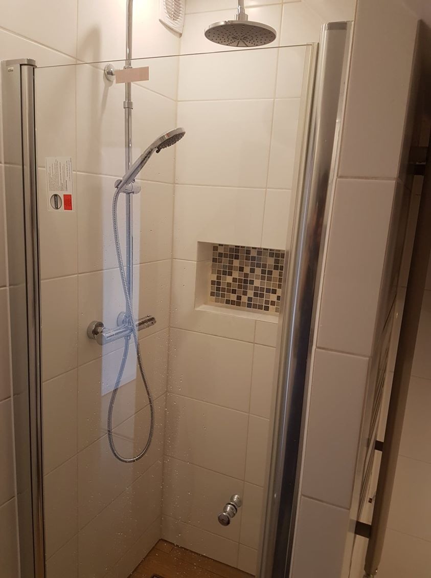 Nowoczesna kabina prysznicowa z deszczownicą i panelem prysznicowym, wykończona beżowymi płytkami i mozaiką w niszy, widoczne krople wody na szklanej ściance.