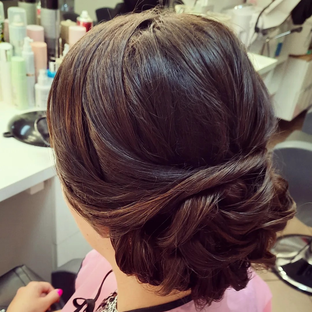 Upięcie z brązowych włosów z delikatnymi refleksami, widok z tyłu, tłem są kosmetyki i lustro.