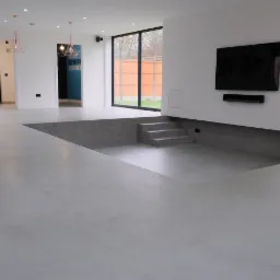 Nowoczesne wnętrze z szarą posadzką żywiczną i obniżonym poziomem podłogi z betonowymi schodami, minimalistyczny design z białymi ścianami i dużym oknem.