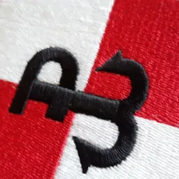 Haftowana naszywka z czarnym, stylizowanym symbolem na czerwono-białym tle w szachownicę.