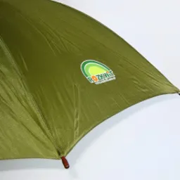 Zielony parasol z nadrukowanym logo firmy w okręgu z motywem górskim, widoczne szprychy i drewniany uchwyt na tle białej ściany.