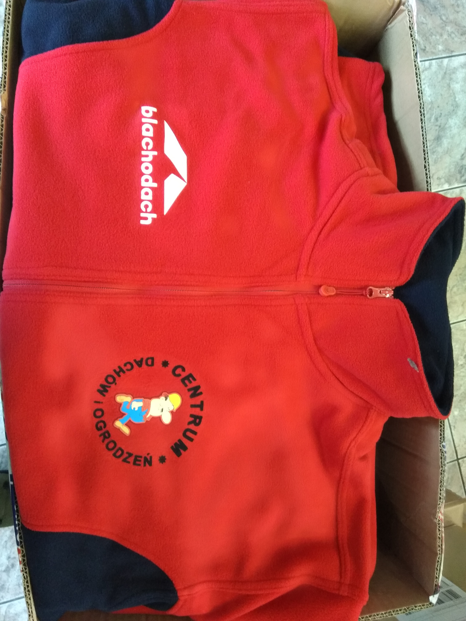 Czerwona polarowa bluza z nadrukowanym logo firmy 'blachodach' i postacią z bajki, zapakowana w karton.