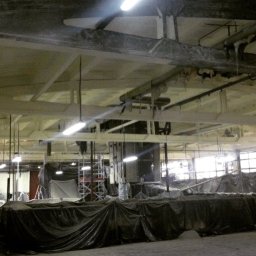 redlabpro specjalistyczne usługi remontowo budowlane - Wnętrze hali przemysłowej w trakcie prac malarskich, zabezpieczone folią, widoczne rusztowania i instalacje pod sufitem.