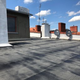 redlabpro specjalistyczne usługi remontowo budowlane - Widok na płaski dach pokryty papą termozgrzewalną z kominami i antenami satelitarnymi w słoneczny dzień.
