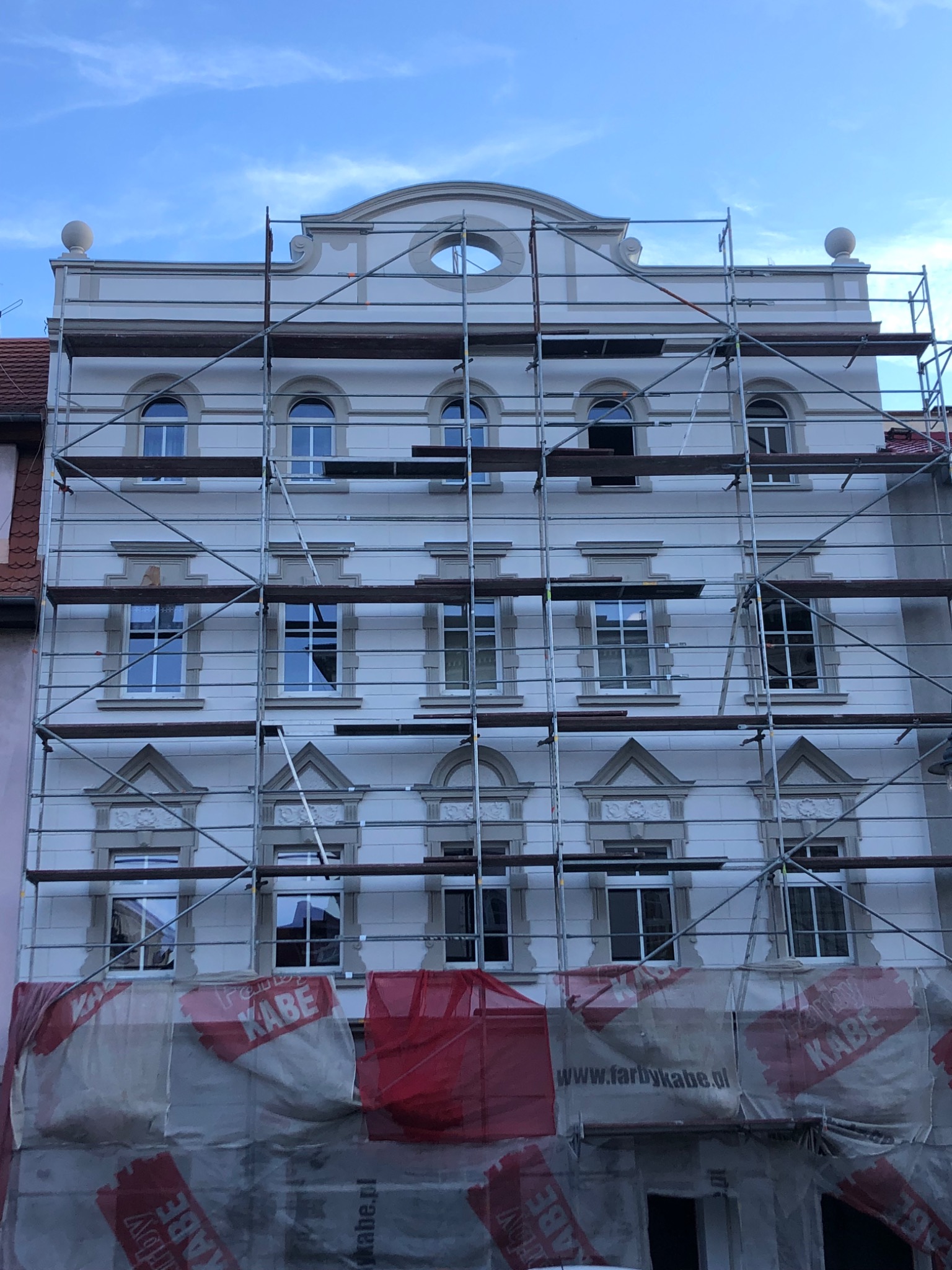 Elewacja kamienicy w trakcie prac remontowych, widoczne rusztowania i folie ochronne z logo producenta farb.