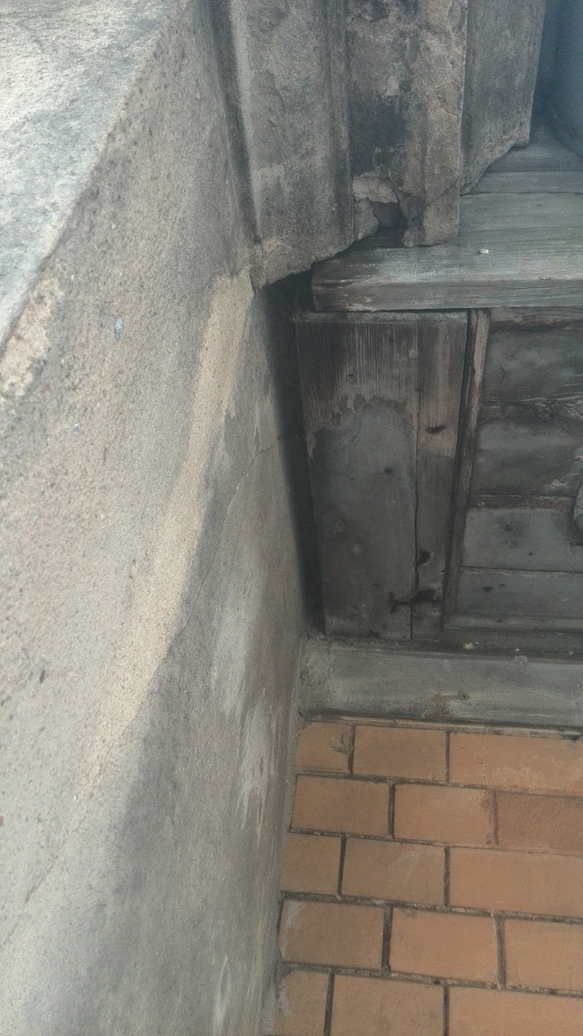 Narożnik budynku z widoczną izolacją fundamentów, ceglaną ścianą i drewnianym fragmentem konstrukcji, ukazujący detale wykonania i wykończenia.