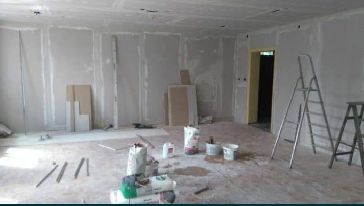 Wnętrze w trakcie wykańczania: ściany obłożone płytami gipsowo-kartonowymi, widoczne szpachlowane łączenia, na podłodze narzędzia, worki z zaprawą i dwie drabiny.