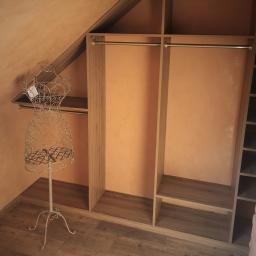 MAGURA - Wnętrze garderoby ze skośnym sufitem, z drewnianą podłogą i metalowym manekinem na ubrania.