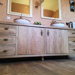 MAGURA - Drewniana szafka łazienkowa z dwoma umywalkami ceramicznymi, stylizowanymi na rustykalne, z dekoracyjnymi, metalowymi kranami i uchwytami, na tle ściany w odcieniach beżu z ramkami zdjęć.