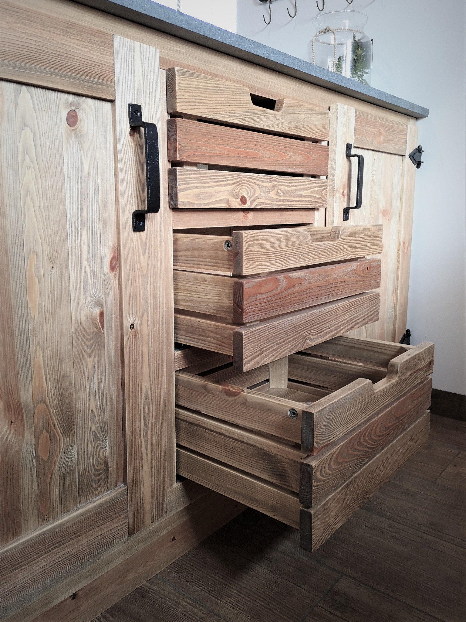 Drewniana komoda z wysuwanymi szufladami-koszykami, wykonana na wymiar w Toruniu, z widoczną strukturą drewna i metalowymi uchwytami.
