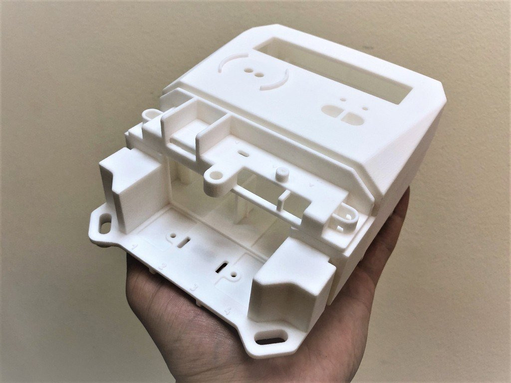 Biały, plastikowy element obudowy z widocznymi otworami montażowymi i wgłębieniami, trzymany w dłoni, prawdopodobnie wykonany metodą druku 3D.