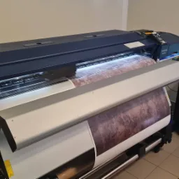 Szerokoformatowa drukarka Epson SureColor SC-S80610 w trakcie drukowania grafiki o teksturze marmuru, widoczny komputer z oprogramowaniem sterującym, obok okno.