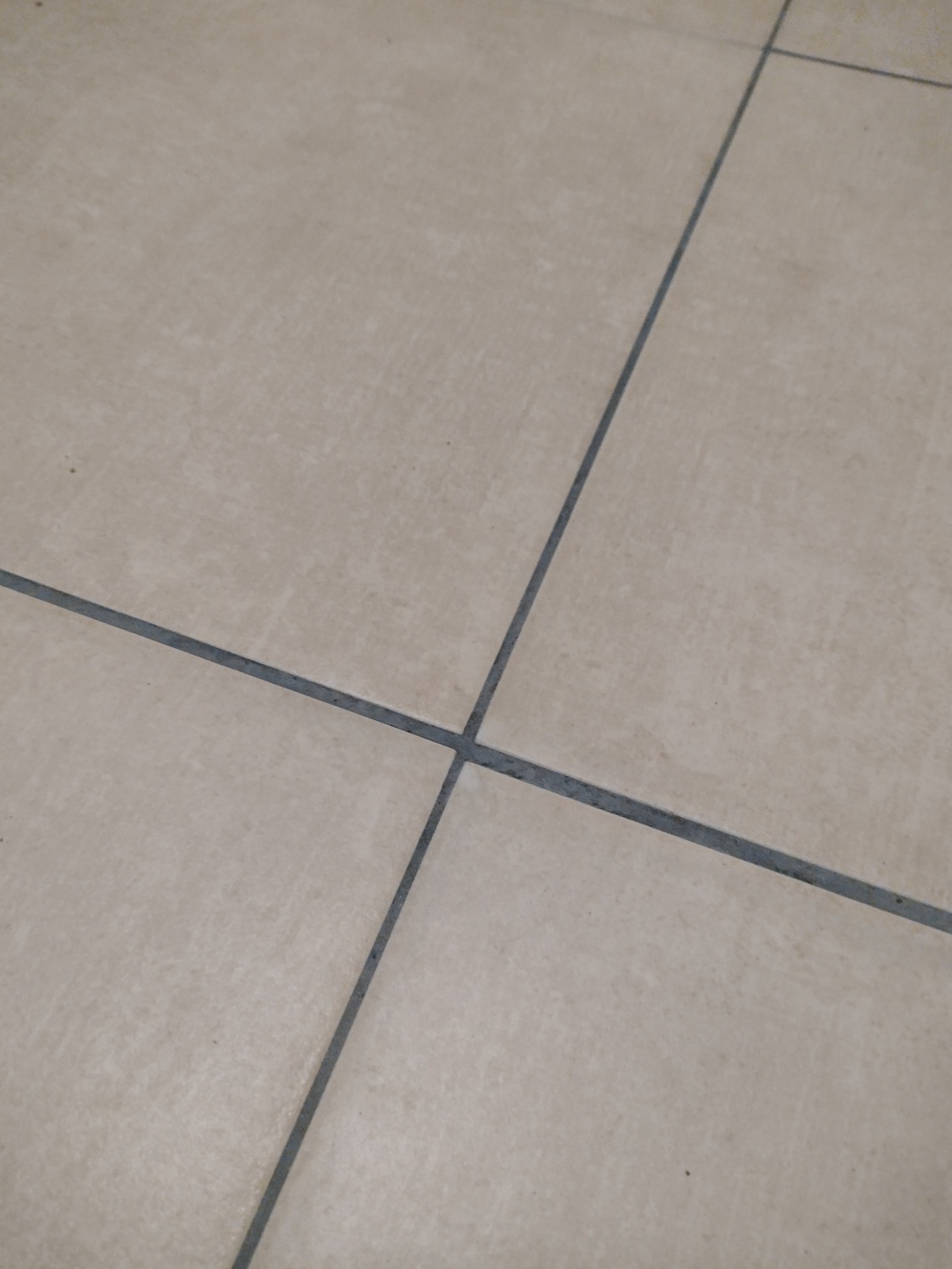 Beżowe płytki podłogowe z ciemnoszarą fugą, ułożone w kwadraty, widok z góry.