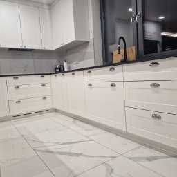 Ewelina Galwiaczek Meble Ni-Na - Nowoczesna, biała kuchnia z marmurowym blatem i podłogą, chromowane uchwyty, czarna bateria kuchenna i okno z czarną ramą.