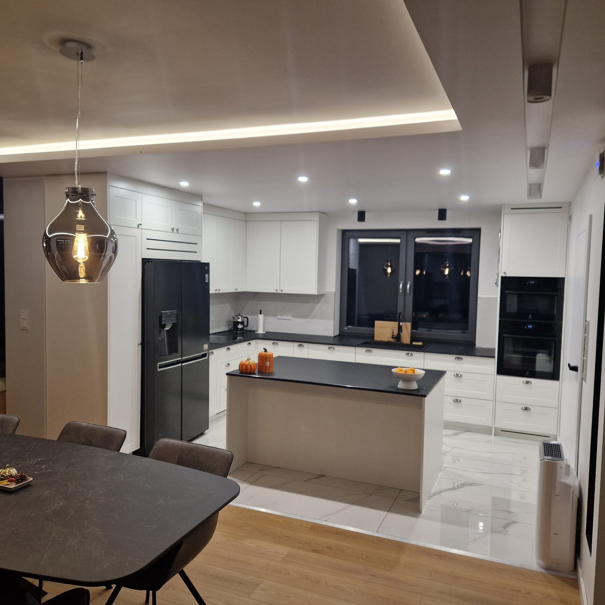 Nowoczesna, jasna kuchnia z wyspą i czarnymi blatami w Radziechowicach Pierwszych, z widoczną lampą wiszącą w stylu retro i elementami dekoracyjnymi na wyspie.