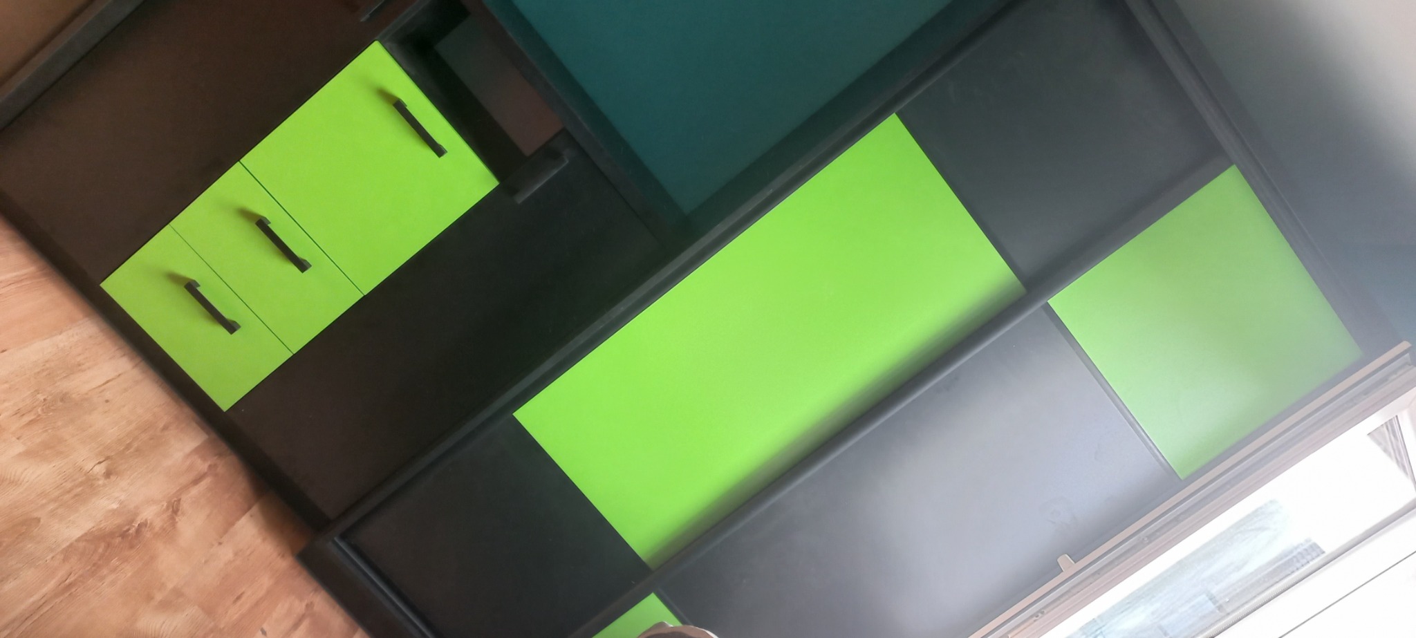 Nowoczesna szafa z geometrycznymi frontami w kolorach czerni, szarości, zieleni i turkusu, uchwyty w kolorze czarnym, widok z dołu.