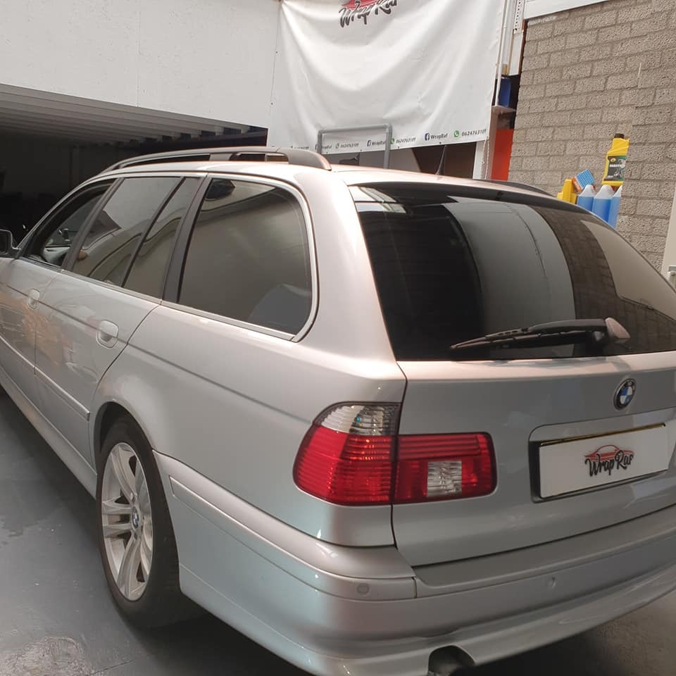 Srebrne kombi BMW serii 5 z przyciemnionymi szybami, widoczne z tyłu, z logo firmy na tablicy rejestracyjnej i banerem reklamowym w tle.